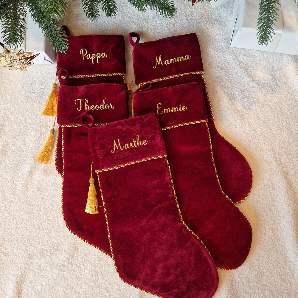 Eksklusiv rød julestrømpe i fløyel med personlig brodert navn “Thomas”. Dekorert med elegant gullfrynse og hengende på juletre med julelys og pynt. Nå med 20 % rabatt hos Eventyrprint.no – perfekt personlig julestrømpe i fløyel til jul. Familie