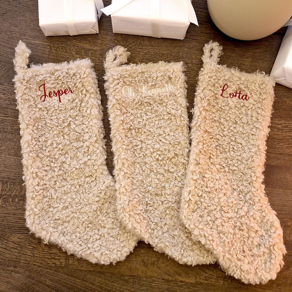 Beige teddy julestrømpe med personlig brodert navn “Jostein”. Myk og fluffy julestrømpe hengende ved juletreet, perfekt til julegaver og pynt. 20 % rabatt hos Eventyrprint.no – design din egen julestrømpe med navn. 3 sokker
