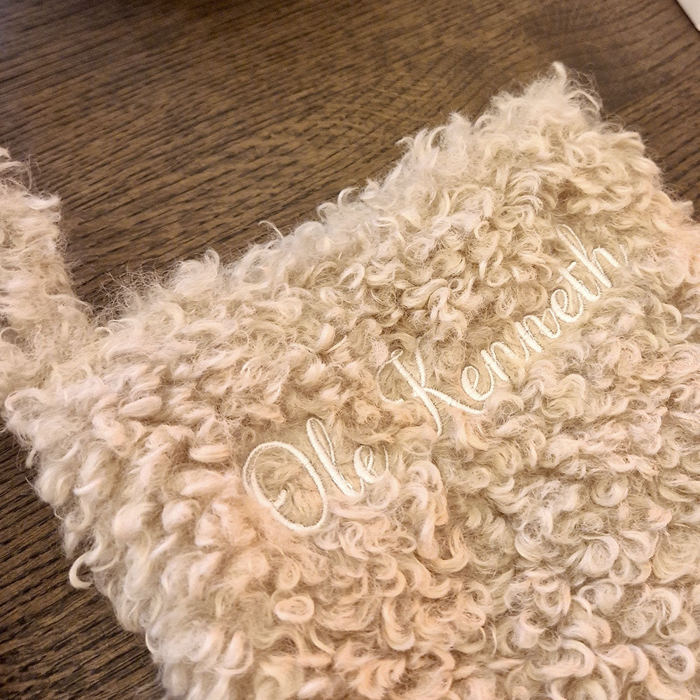 Beige teddy julestrømpe med personlig brodert navn “Jostein”. Myk og fluffy julestrømpe hengende ved juletreet, perfekt til julegaver og pynt. 20 % rabatt hos Eventyrprint.no – design din egen julestrømpe med navn. Nærbildet