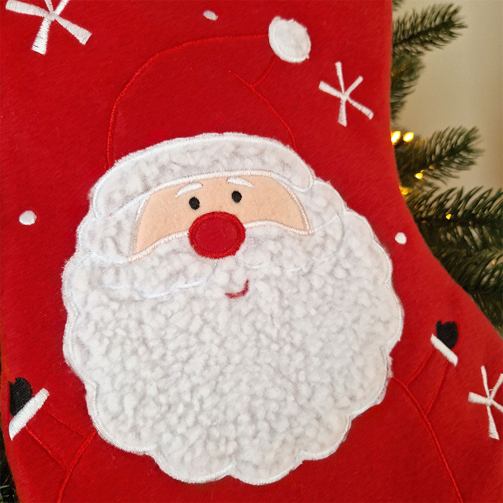 Rød julestrømpe med hvit mansjett og brodert navn, dekorert med stor julenisse og snøfnuggmotiv. Nærbildet av motiv