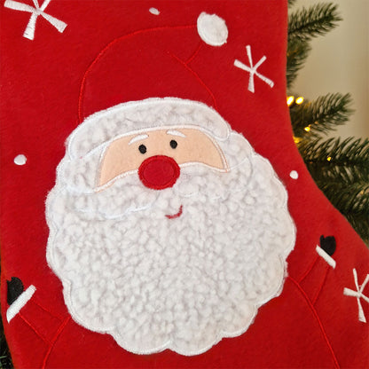 Rød julestrømpe med hvit mansjett og brodert navn, dekorert med stor julenisse og snøfnuggmotiv. Nærbildet av motiv